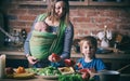 Happy young family, beautiful mother with two children, adorable preschool boy and baby in sling cooking together in a sunny kitch Royalty Free Stock Photo