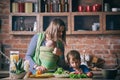 Happy young family, beautiful mother with two children, adorable preschool boy and baby in sling cooking together in a sunny kitch Royalty Free Stock Photo