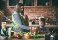 Happy young family, beautiful mother with two children, adorable preschool boy and baby in sling cooking together in a sunny kitch Royalty Free Stock Photo