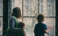 Happy young family, beautiful mother with two children, adorable preschool boy and baby in sling look together through the window