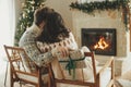 Happy young family in cozy sweaters exchanging stylish christmas gifts on background of fireplace with modern festive mantle and