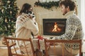 Happy young family in cozy sweaters hugging with cute cat and exchanging stylish christmas gifts on background of fireplace with Royalty Free Stock Photo