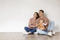 Happy Young Family With Cute Baby Sitting On Floor And Looking Aside Royalty Free Stock Photo