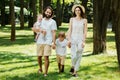 Happy young family dressed in the white casual clothes walks in the park on a sunny summer day. Royalty Free Stock Photo