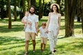 Happy young family dressed in the white casual clothes walks in the park on a sunny summer day. Royalty Free Stock Photo