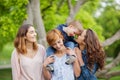 Happy young family enjoying free time in the park, mother, sisters and brother