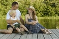 Happy young family, father mother and little blond son are sitting on the river pier Royalty Free Stock Photo