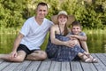 Happy young family, father mother and little son are sitting on the river pier Royalty Free Stock Photo