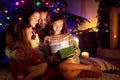 Happy young family of four using a tablet pc at home by a fireplace in warm and cozy living room on Christmas eve Royalty Free Stock Photo