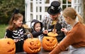 Happy young family in Halloween costumes carving pumpkins together in backyard