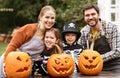 Happy young family in Halloween costumes carving pumpkins together in backyard