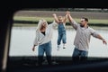 Happy Young Family Having Fun Outdoors, Mom and Dad Taking Up Their Little Daughter by Hands, View Through Window Inside Royalty Free Stock Photo