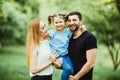 Happy young family spending time together in green nature. wife with husbend and daughter. Mother and father holding daughter in p