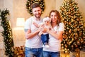 Happy young family standing near Christmas tree in living room while holding little cute baby girl Royalty Free Stock Photo