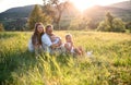 Young family with two small children sitting on meadow outdoors at sunset. Royalty Free Stock Photo