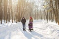 Happy young family walking in the park in winter. The parents carry the baby in a stroller through the snow. Royalty Free Stock Photo