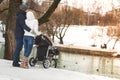 Happy young family walking in a winter park, mom, dad and son in stroller. Royalty Free Stock Photo