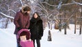 Happy, young family walking in a winter park, mom, dad and baby in pink stroller. Man pointing the finger and parents Royalty Free Stock Photo