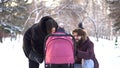 Happy, young family walking in a winter park, mom, dad and baby in stroller. Smiling parents leaning over pink stroller Royalty Free Stock Photo