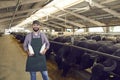 Happy young farmer standing in barn, holding bottles of natural cow milk and looking at camera