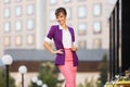 Young fashion business woman in purple blazer and pink skirt walking in city street Royalty Free Stock Photo