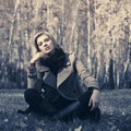 Happy young fashion woman in beige coat sitting on grass outdoor Royalty Free Stock Photo