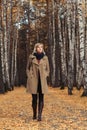 Happy young fashion woman in beige coat walking in autumn park