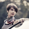 Happy young fashion woman in striped tank top leaning on her car Royalty Free Stock Photo