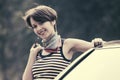 Happy young fashion woman in striped tank top leaning on her car Royalty Free Stock Photo