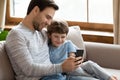 Happy young father cuddling little son, showing funny mobile applications. Royalty Free Stock Photo