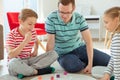 Happy young father plays with his two cheerful siblings children Board Game with colorful dices Royalty Free Stock Photo