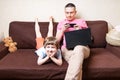 Happy young father sit on couch using laptop relax with kid son holding smartphone have fun together, smiling dad and Royalty Free Stock Photo
