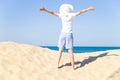 Happy young female arms apart wearing a white hat with a wide brim enjoying life on the sandy beach by the se