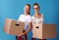 Happy young female roommates holding cardboard boxes on blue