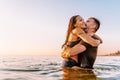Happy young fit couple in sea or ocean hug each other with love at summer sunset. Romantic mood, tenderness