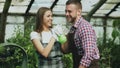 Happy young florist couple in apron have fun while working in greenhouse. Laughing woman spray water in husband face Royalty Free Stock Photo