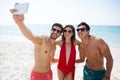 Happy young frends taking selfie through mobile phone at beach