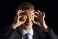 Happy young funny attractive businessman trader holding bitcoin cryptocurrency instead of eyes,  on black Royalty Free Stock Photo