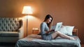 Happy young girl chatting using laptop relaxing at cosiness bedroom having positive emotion