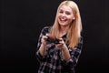 A happy young girl in a checkered shirt, fascinated by a joystick playing a game console and smiling.