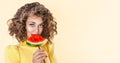 Happy young girl with curly hair holding slice of a watermelon at her face isolated over yellow background. Afro girl holds Royalty Free Stock Photo