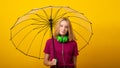 Happy young girl in green headphones, dressed in a lilac T-shirt, holds an umbrella on a yellow background. Bright autumn concept Royalty Free Stock Photo