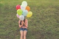 Happy young girl holding colorful balloons and sitting on grass field Royalty Free Stock Photo