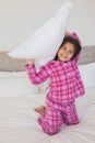 Happy young girl holding up a pillow in bed