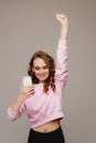 A happy young girl holds the phone looks into it and smiles holding her hand up Royalty Free Stock Photo