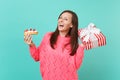 Happy young girl in knitted pink sweater holding eclair cake red striped present box with gift ribbon isolated on blue Royalty Free Stock Photo
