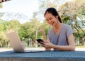 Happy young girl with a phone in her hands working on a laptop at the table in the park. The concept of shopping online in the Royalty Free Stock Photo