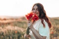 Happy young girl with a poppy bouquet in her hands in a summer field at sunset. Woman looking at the camera Royalty Free Stock Photo