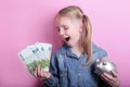 Happy young girl with silver piggy bank and euro banknotes  on pink background. save money concept. Royalty Free Stock Photo