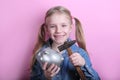 Happy young girl with silver piggy bank  and hammer on pink background. save money concept. Royalty Free Stock Photo